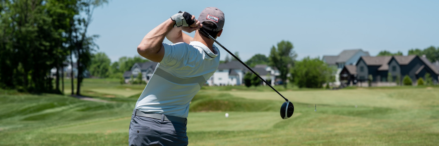 Golfer in follow-through pose after a powerful swing, with golf ball soaring over the fairway in the distance.